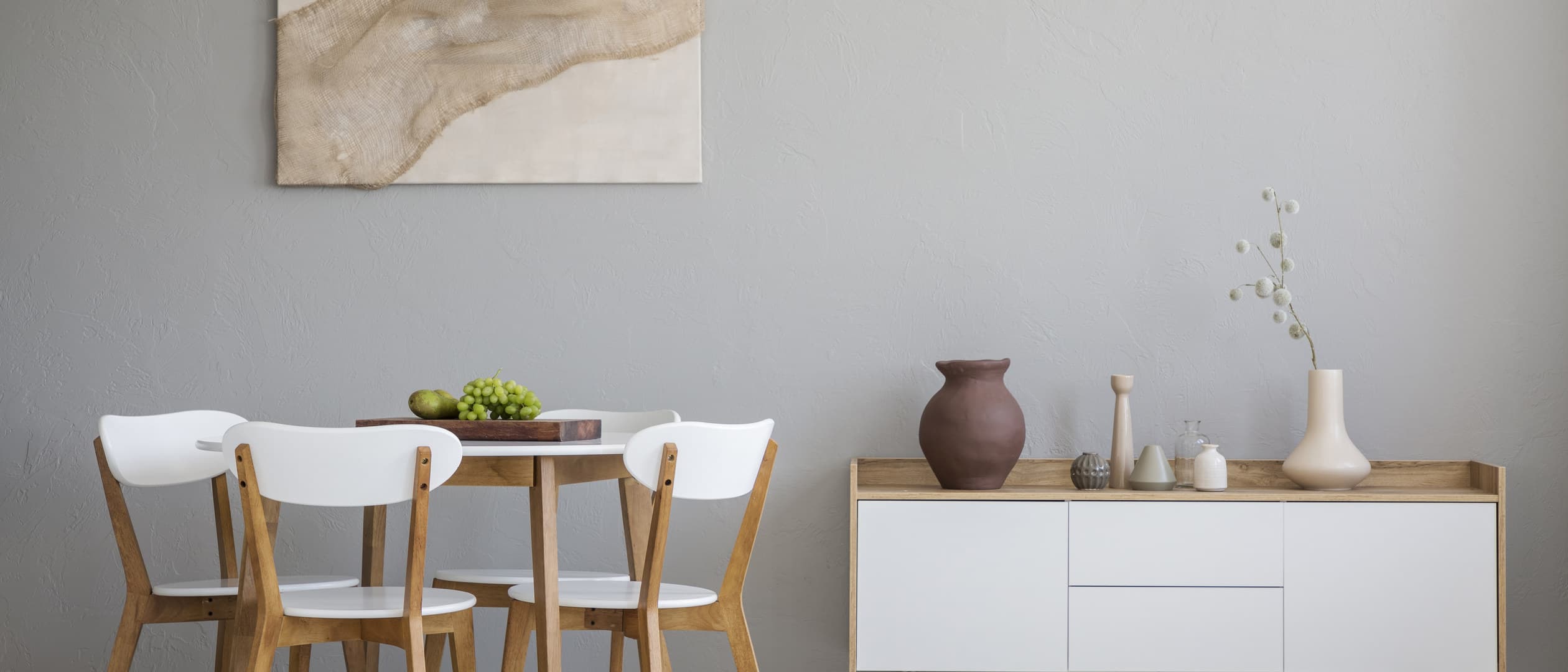 A round pale-wood dining table in daylight, with curved-back chairs and a white pendant.