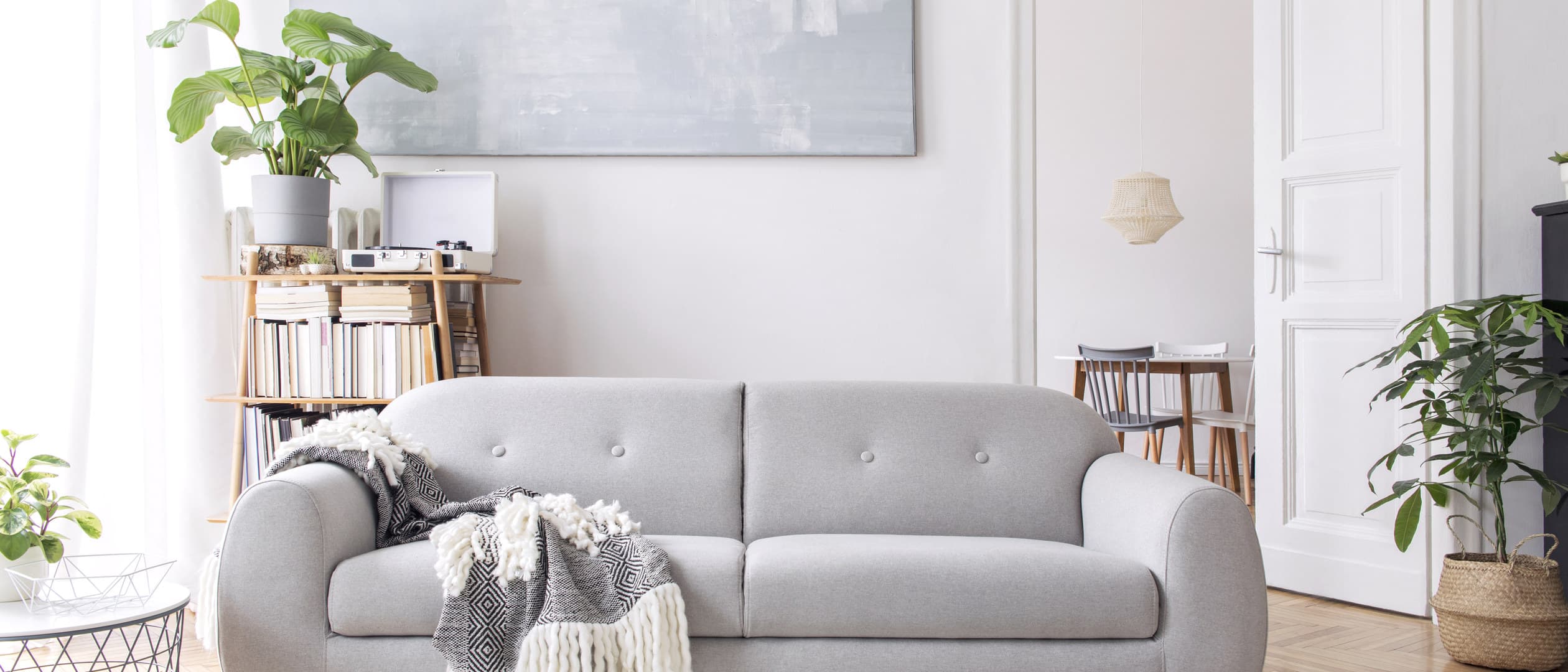 A low beige sofa in a bright living room, with a round ottoman and a slim coffee table.