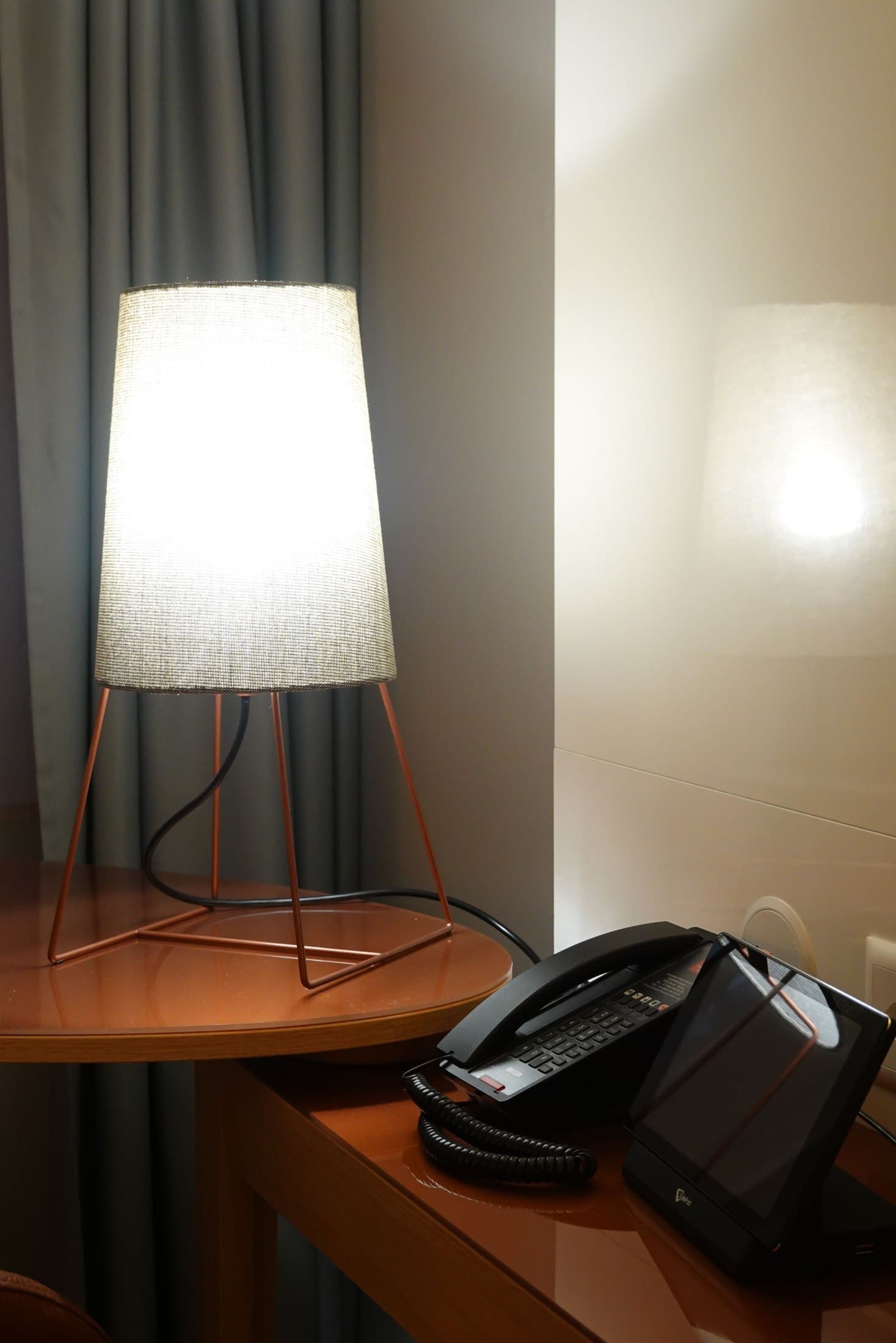 Compact hotel desk with a lamp, telephone and curtain