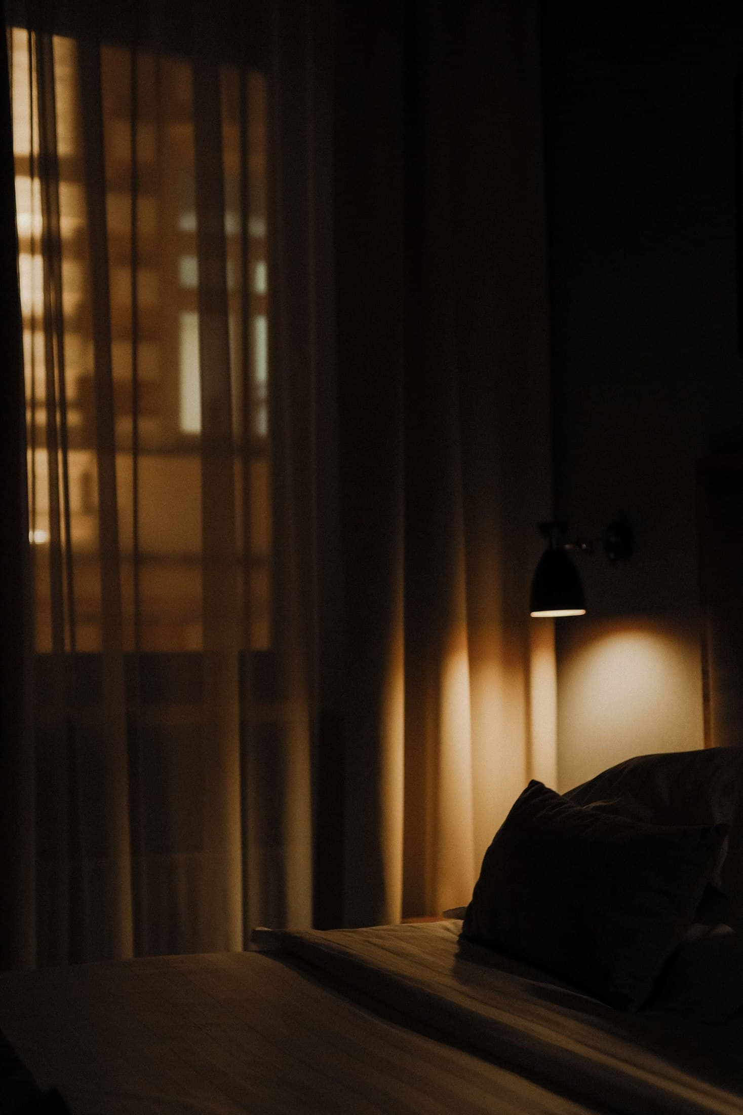 Dark hotel bedroom with full curtains and a focused reading light