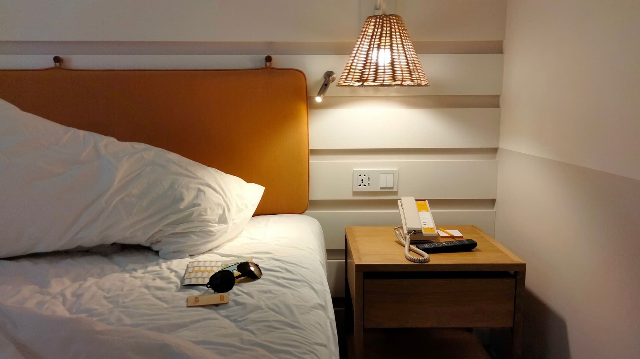 Hotel nightstand with a woven lamp, telephone and practical controls