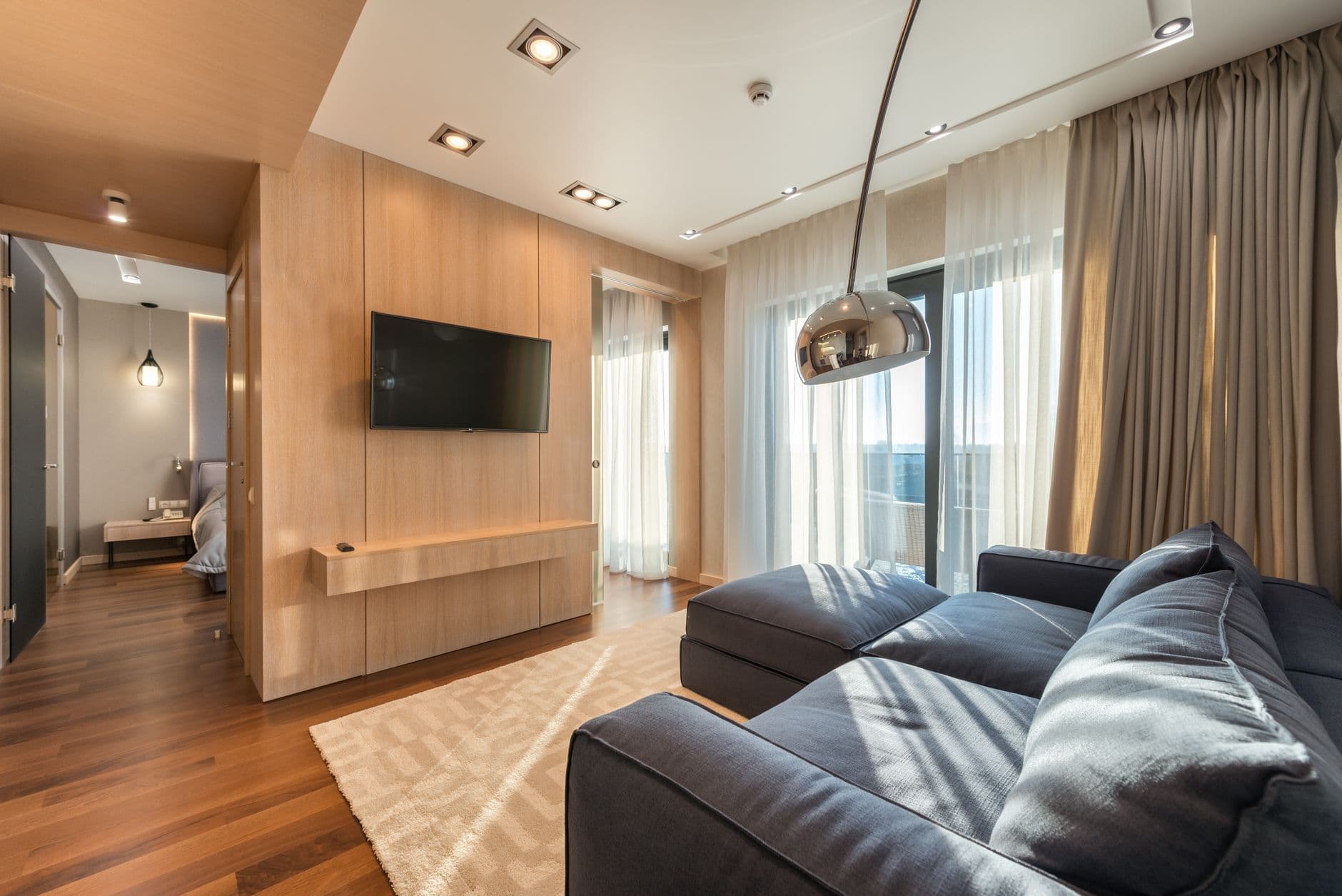 Modern apartment living room with a full pale timber wall, dark sofa and restrained furniture