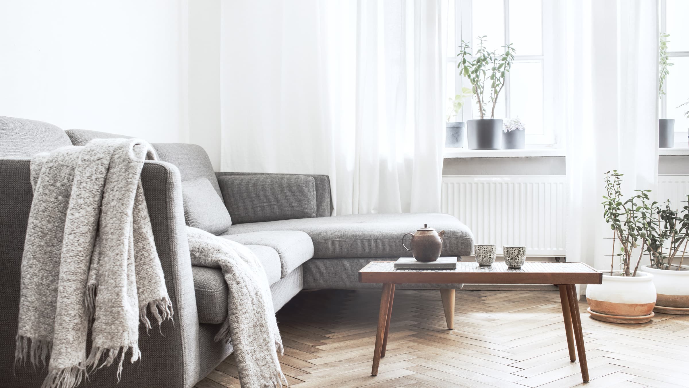Woonkamer in daglicht met een grijze bank en een eiken salontafel